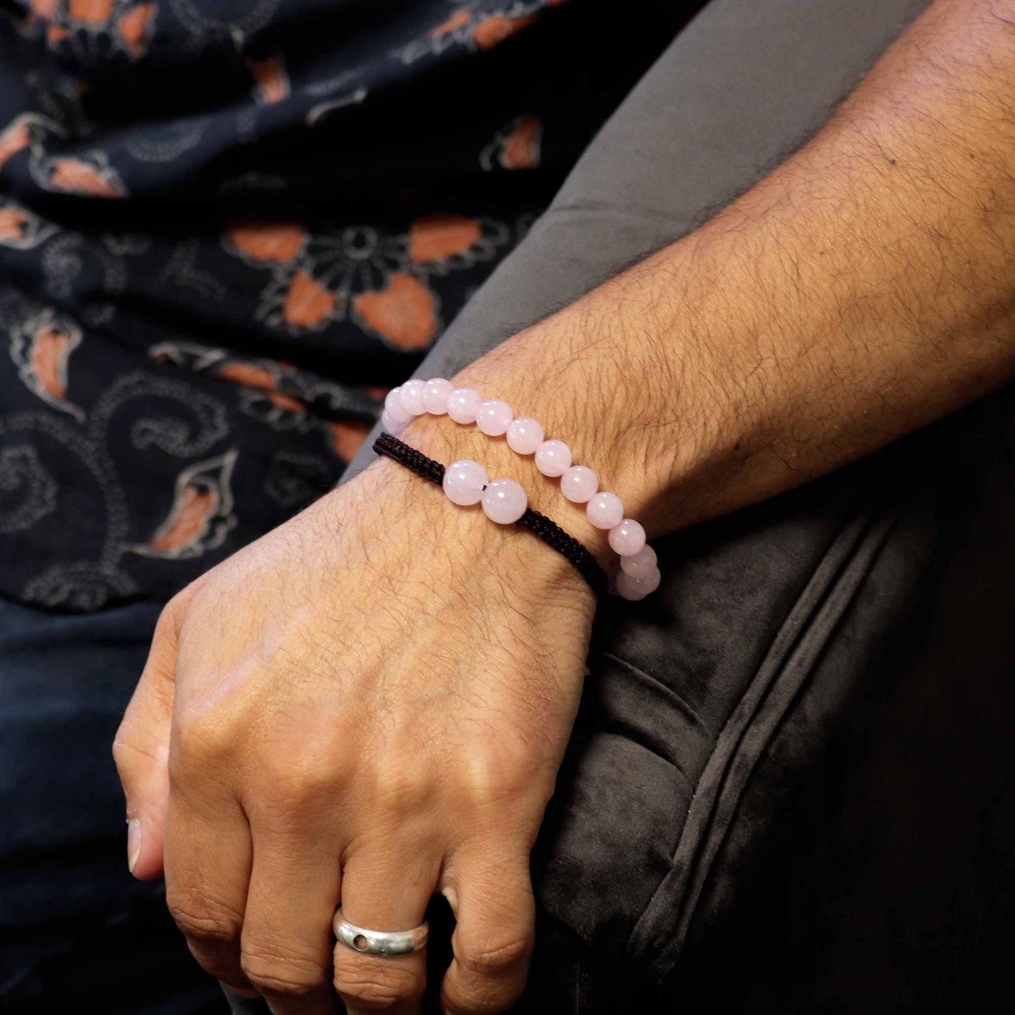 Close-up of a wrist wearing a pink beaded bracelet with a dark fabric background.