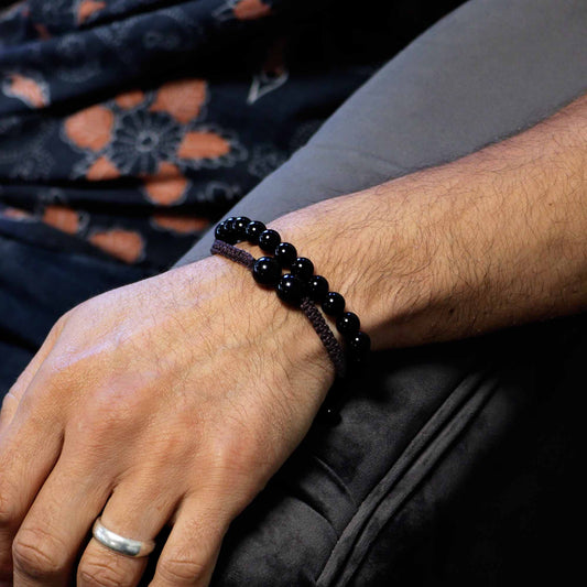 Hand wearing a black beaded bracelet with a blurred background