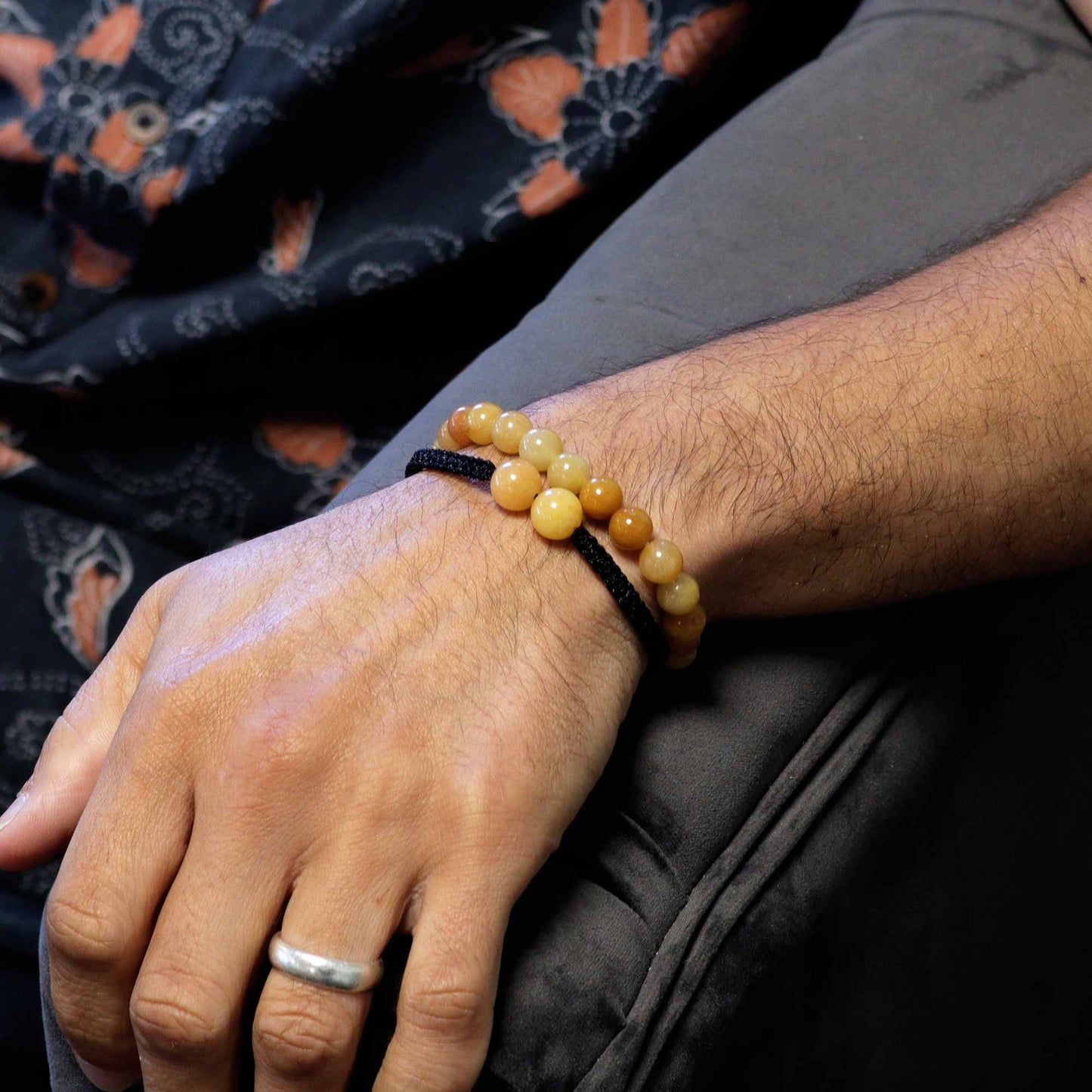 Close-up of a hand wearing a beaded bracelet with a ring on a dark fabric background