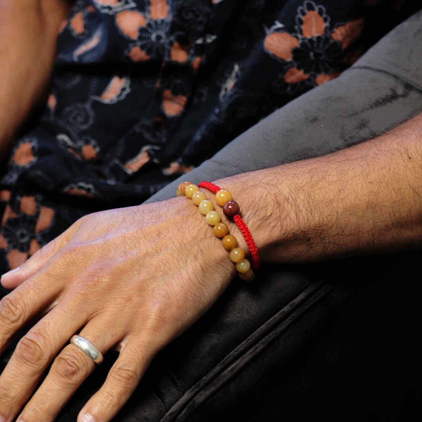 Close-up of a hand wearing a red string bracelet with beads on a dark background