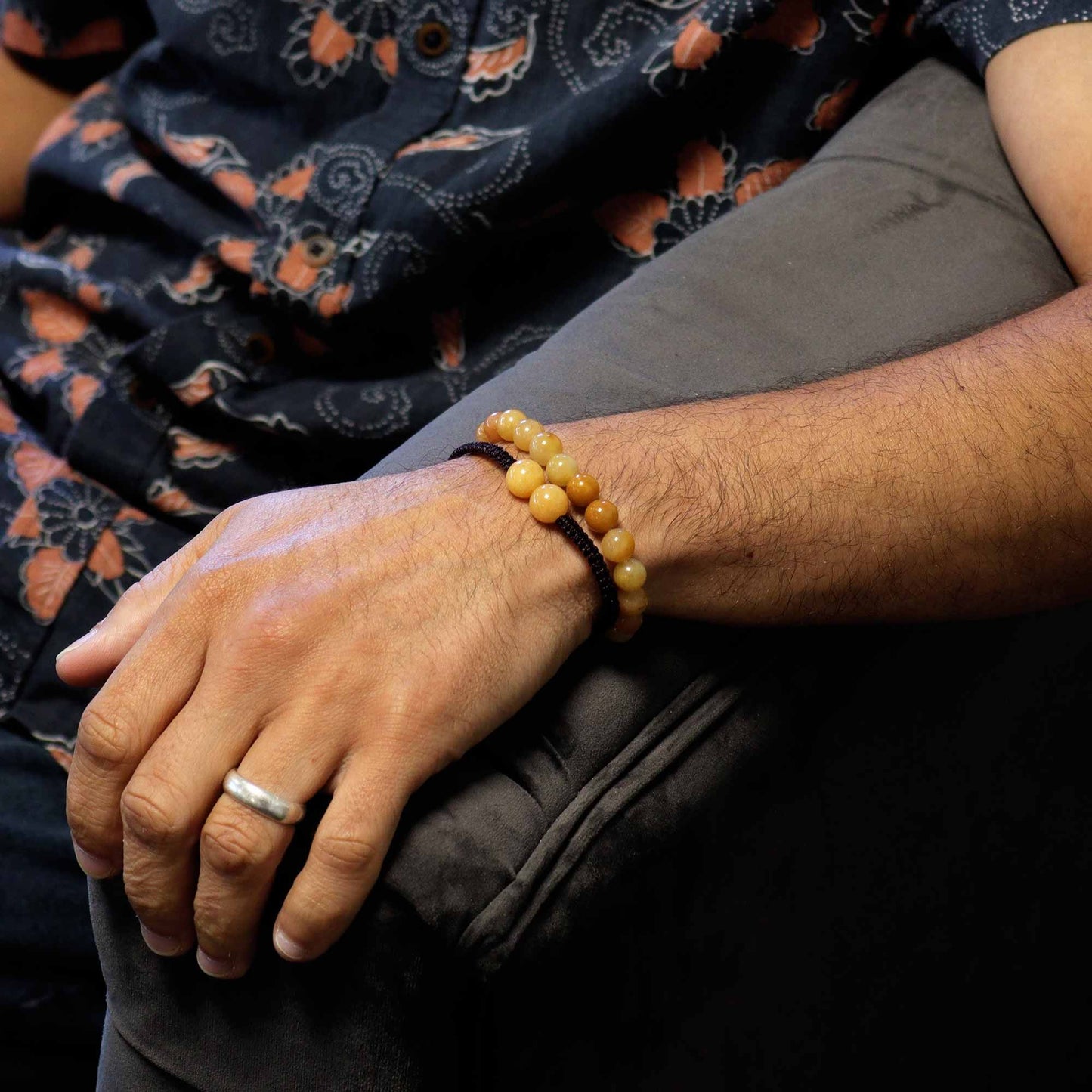 Close-up of a person's wrist with a beaded bracelet and ring, wearing a patterned garment.