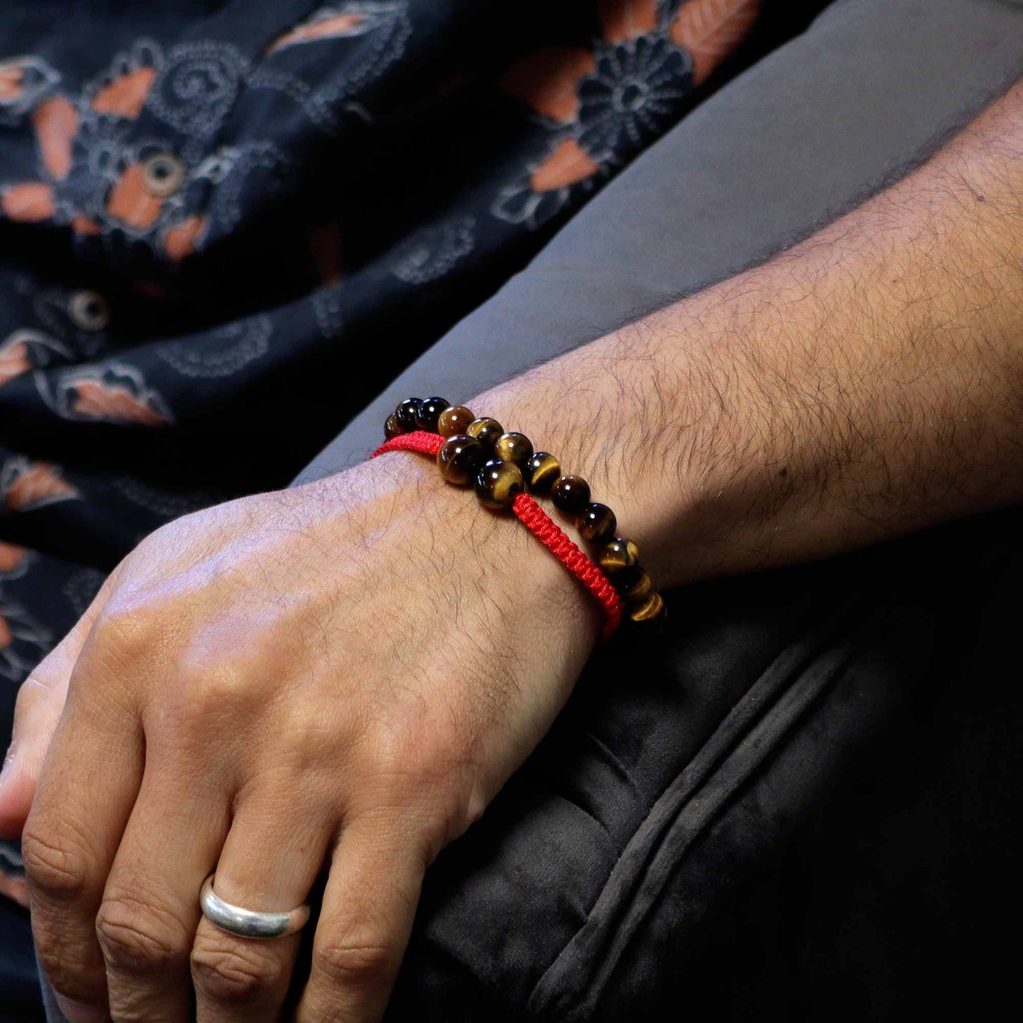 Hand wearing a red string bracelet with beads, with a dark fabric background.