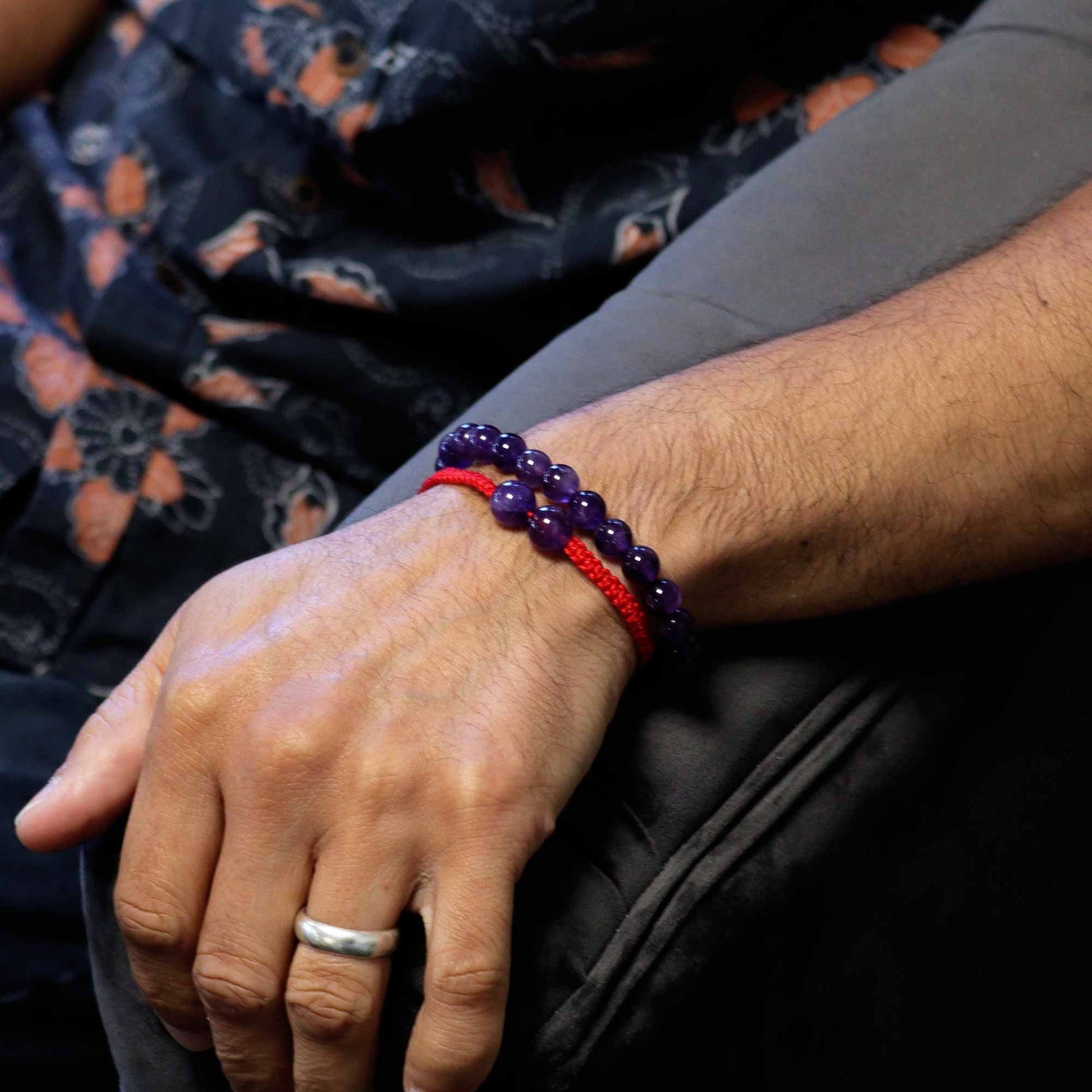 Hand wearing a purple beaded bracelet with a red accent, sitting on a patterned fabric surface.