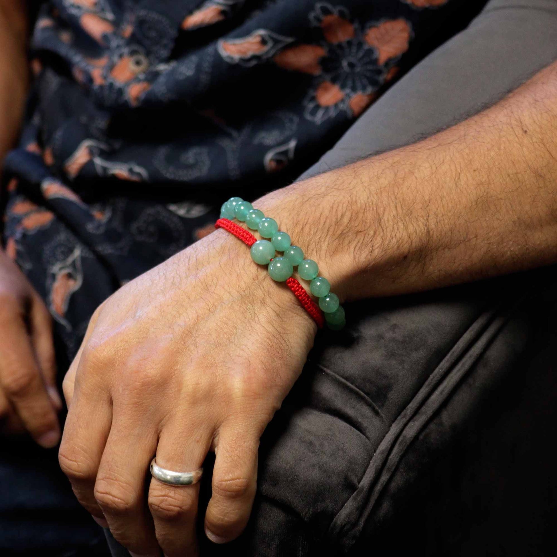 Person wearing a green beaded bracelet with red string on wrist